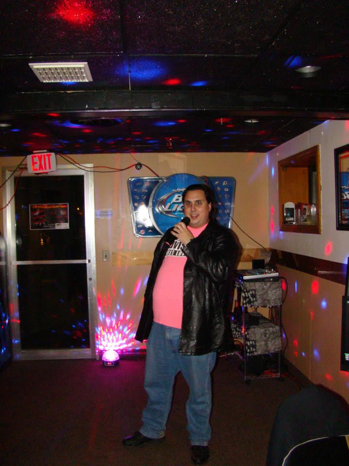 Marco stands in the corner of a bar or cafe holding a microphone and performing