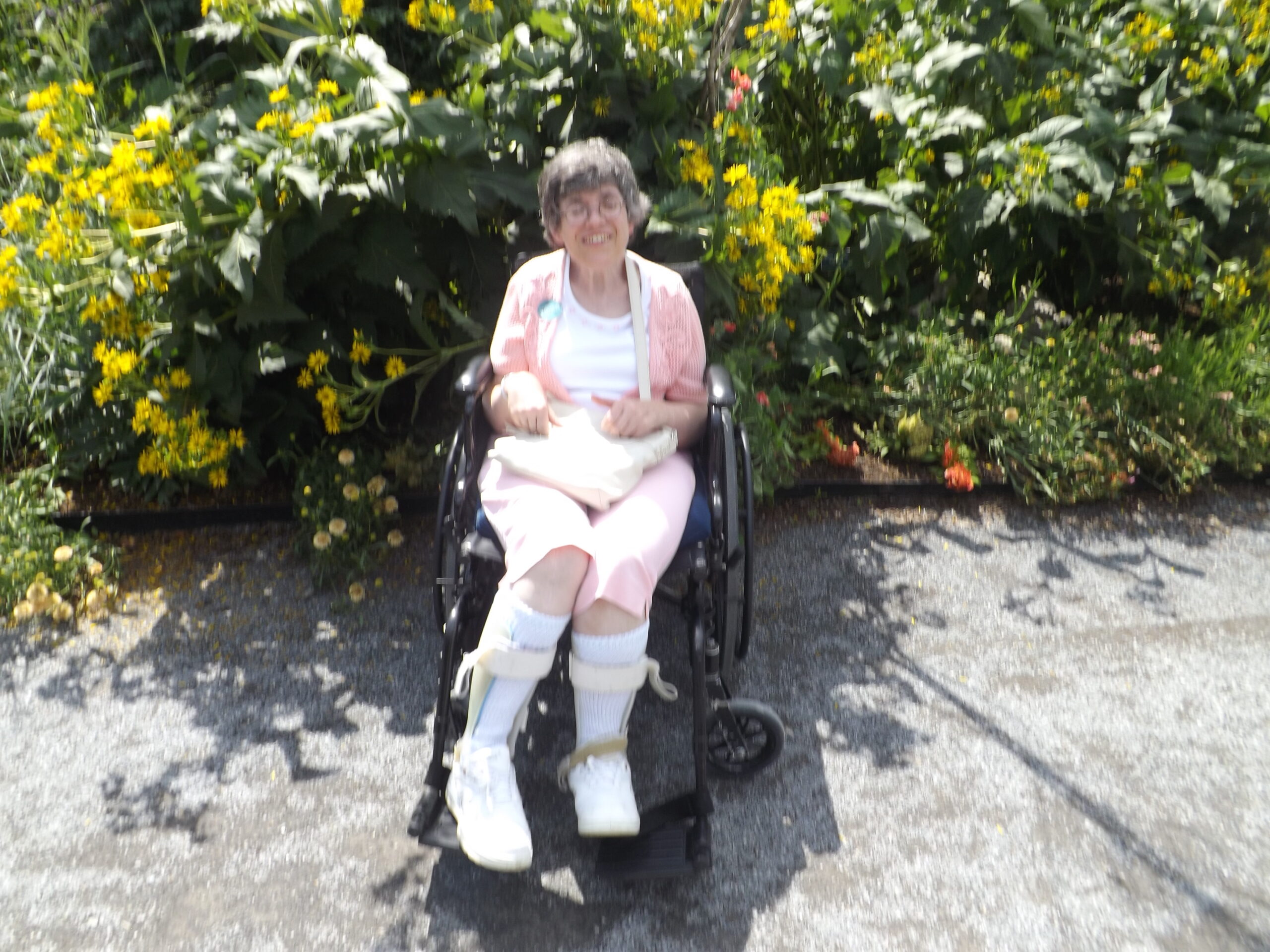 Sarah sits in her powered wheelchair at the botanical garden, in front of a swath of flowers and leaves