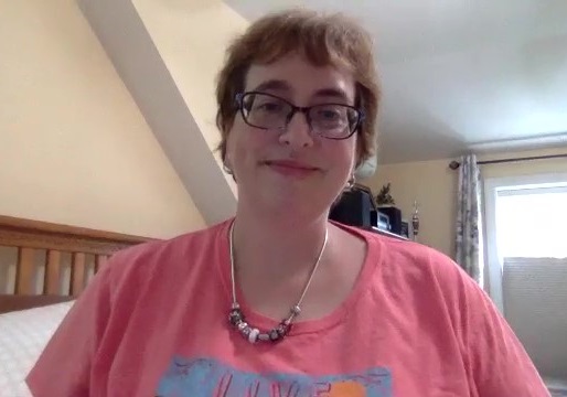 Stacy Smart smiles at the camera, wearing a pink shirt and glasses