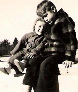 Bobby and Vicki Schad as children - a black and white photograph of two children sitting together with the larger one holding the smaller one close